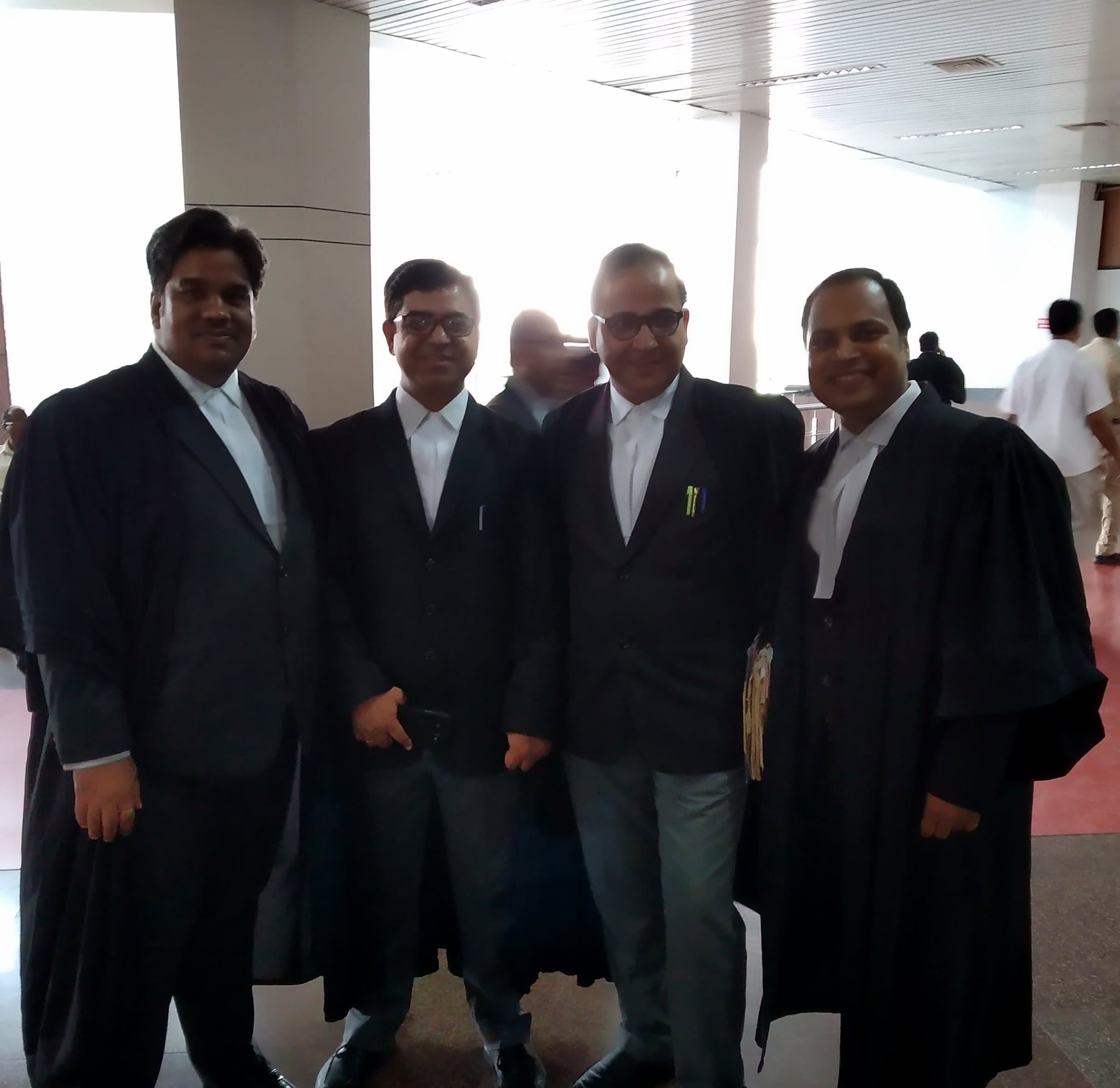 Four advocates of the firm in gowns and bands, standing together in the hall of a court building