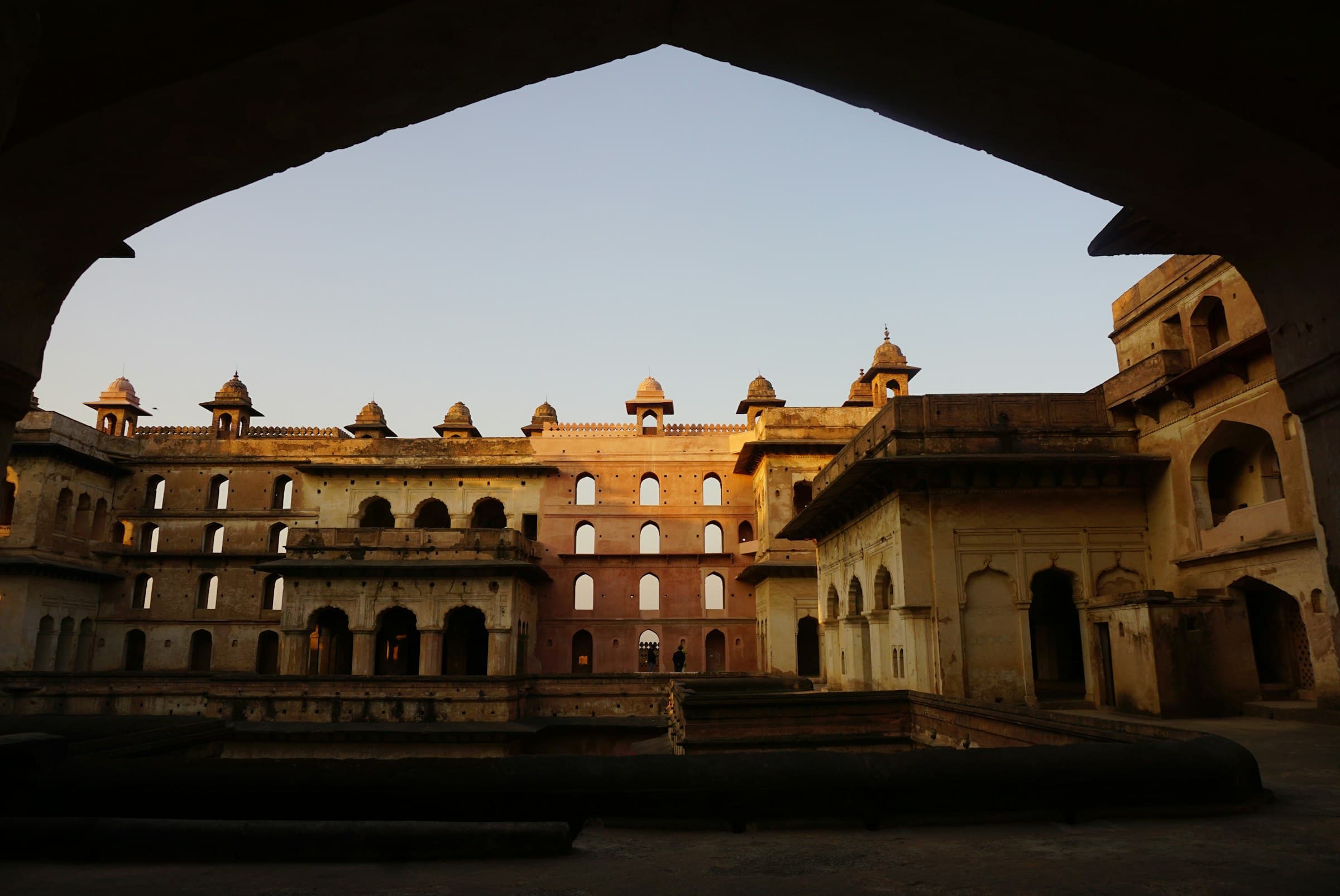 A dark stone arch framing a sandstone palace at dusk
